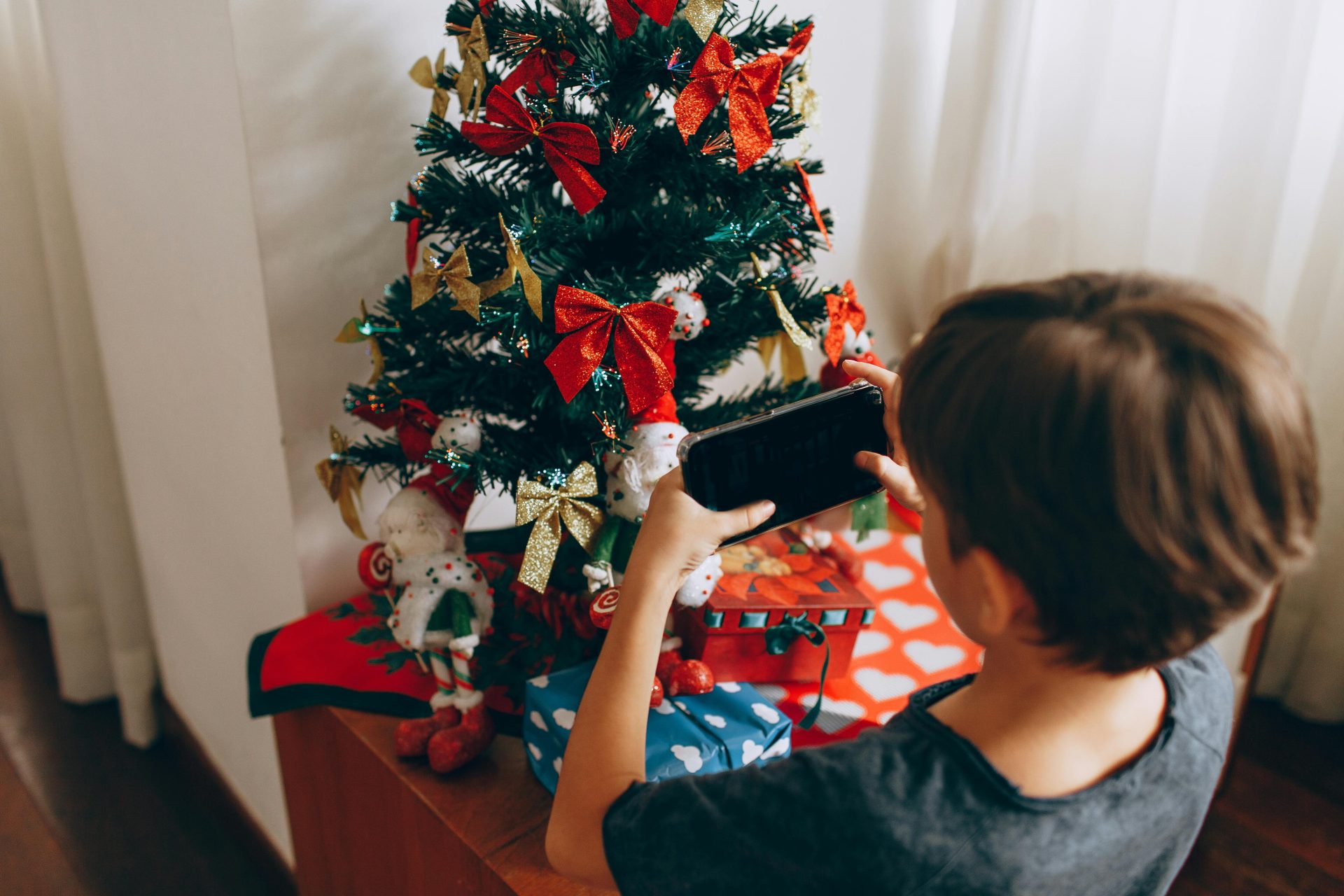 Kind mit Smartphone vor Weihnachtsbaum