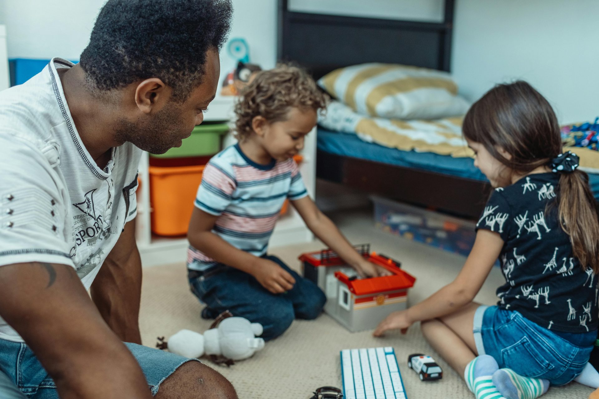 2 enfants jouent ensemble avec un homme adulte, normalement le père, au sol de la chambre d'un enfant avec du playmobil